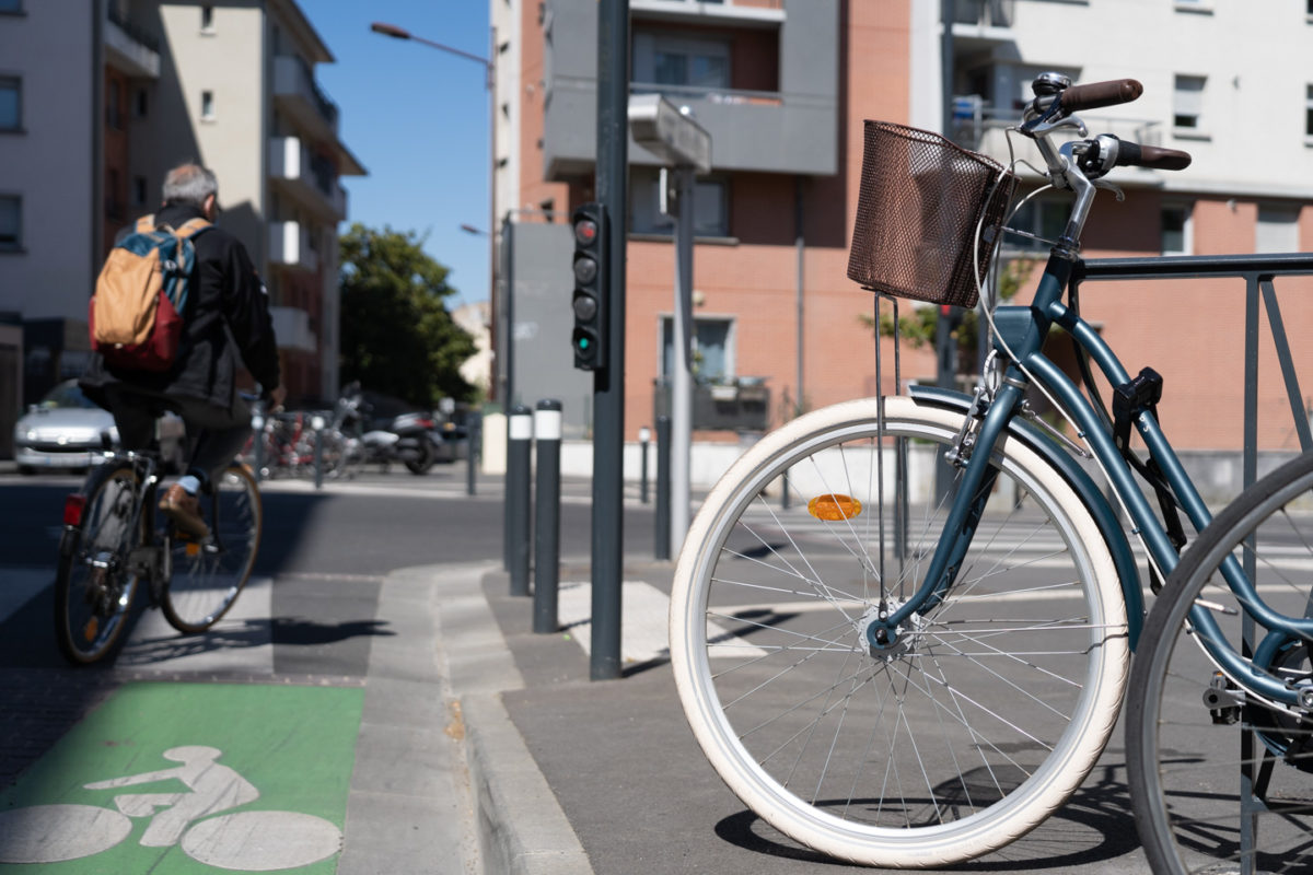 Un vélo de ville est garé à côté du piste cyclable à Toulouse tandis qu'un cycliste s'apprête à prendre un carrefour. Toulouse, le 23 avril 2021.